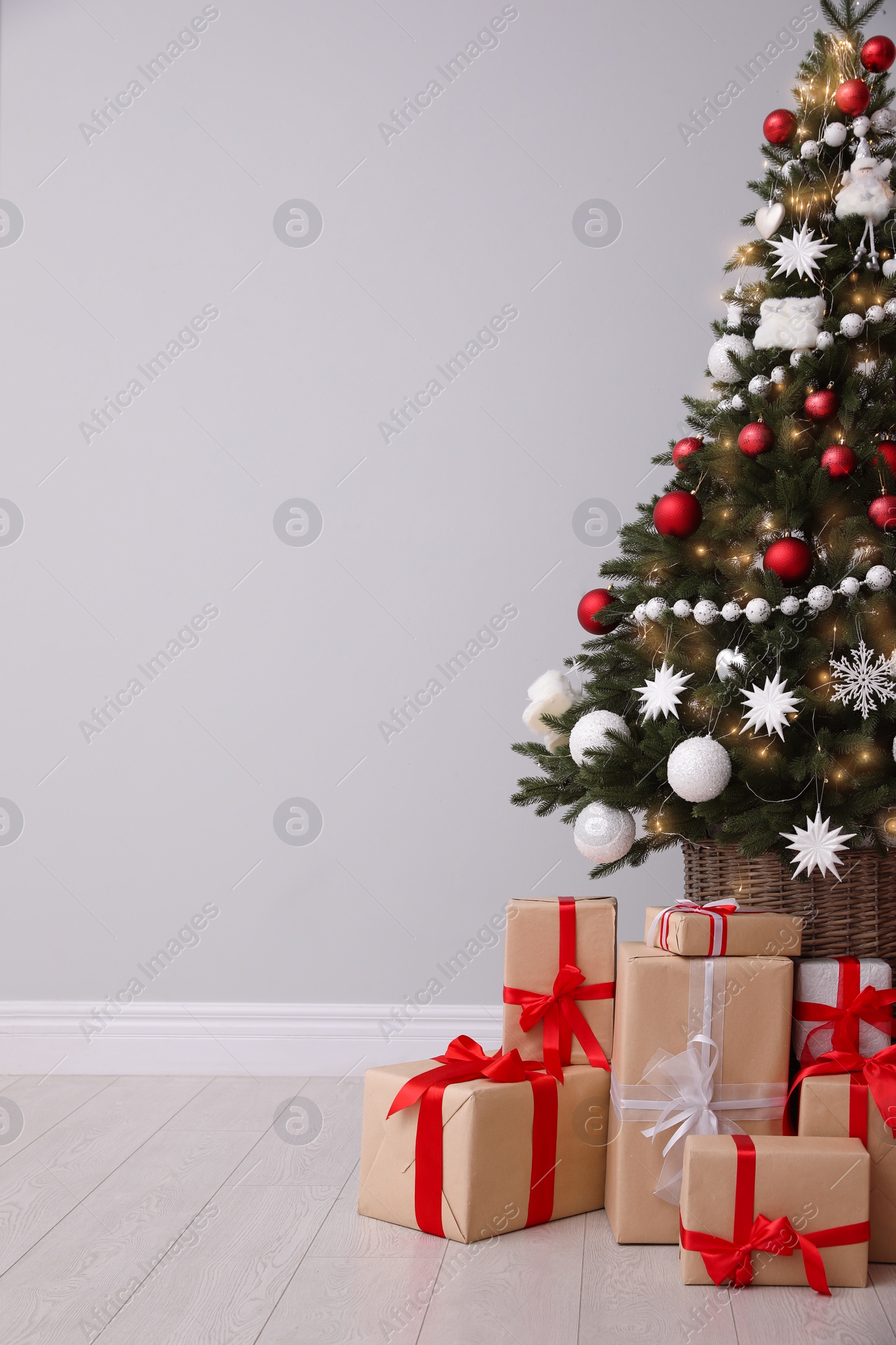 Photo of Christmas tree and gift boxes near light grey wall, space for text