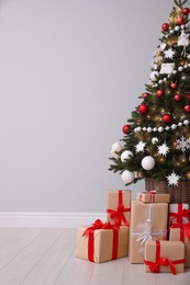 Photo of Christmas tree and gift boxes near light grey wall, space for text
