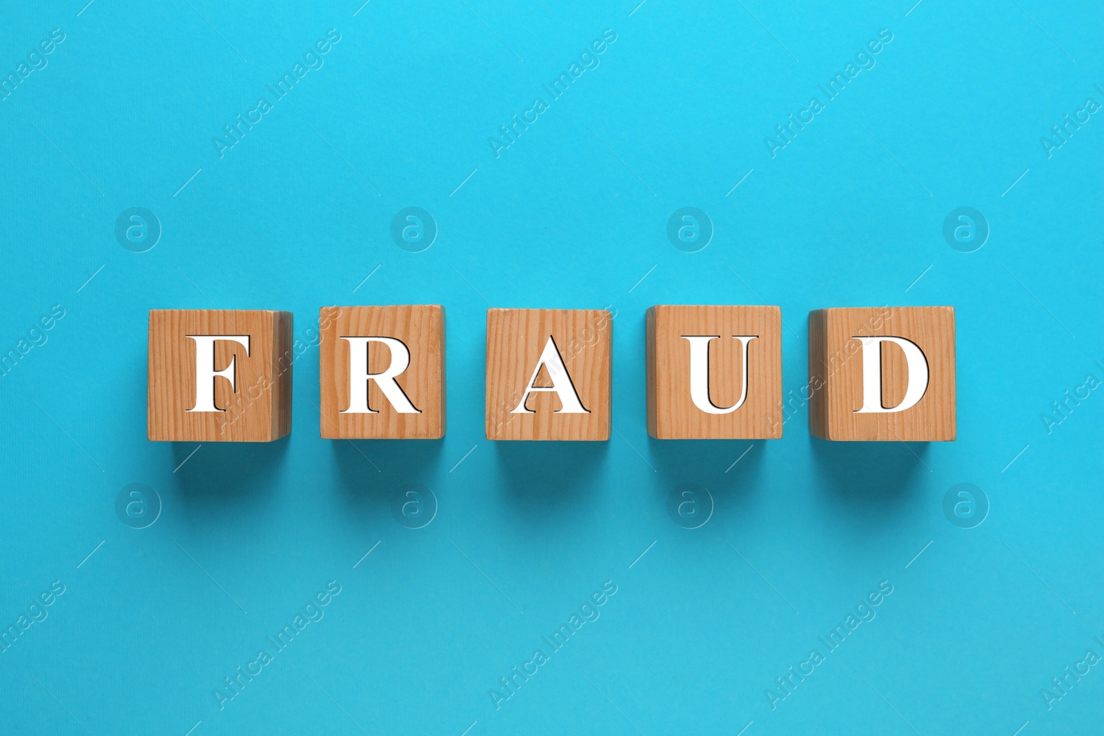 Photo of Wooden cubes with word Fraud on light blue background, flat lay