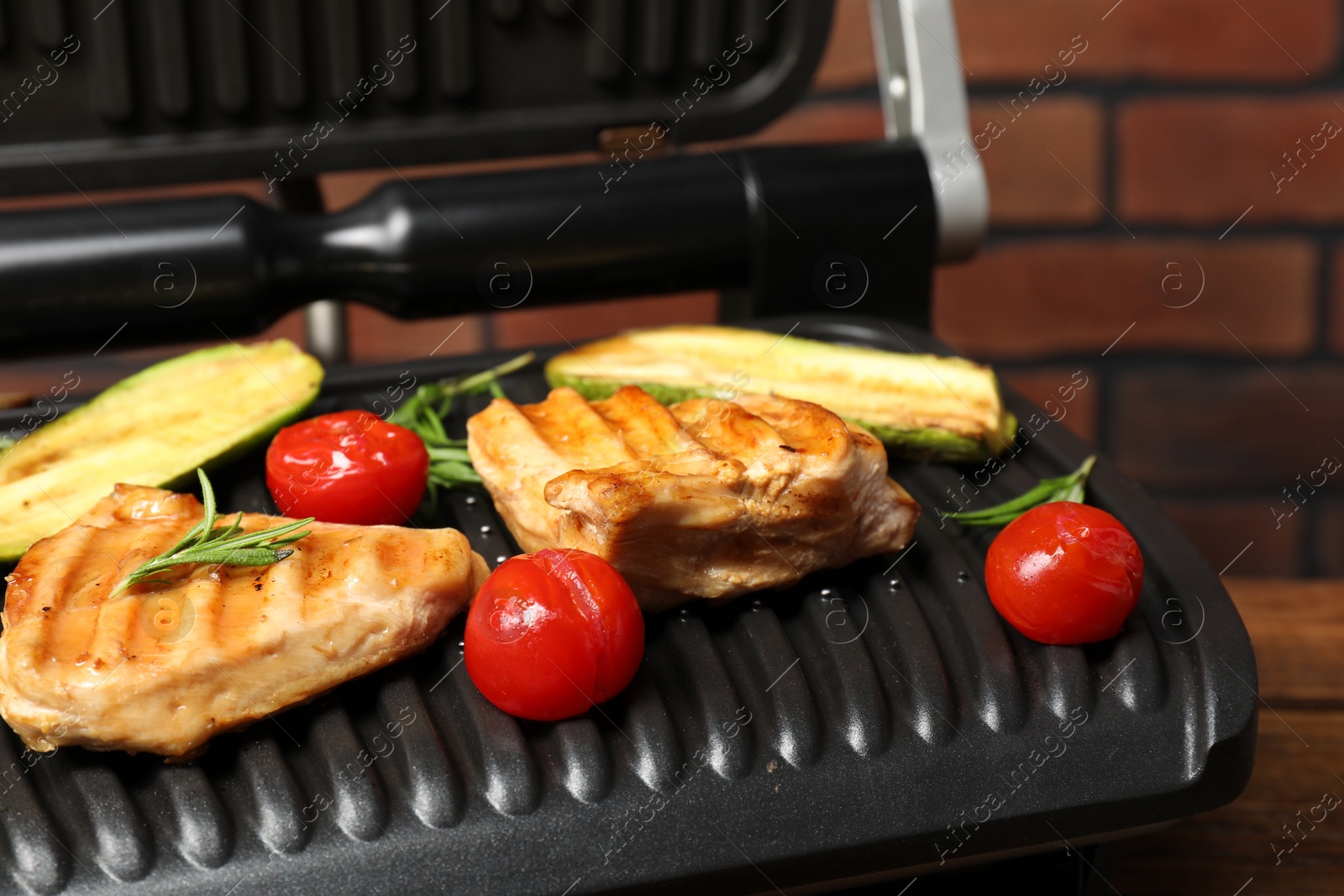 Photo of Electric grill with tasty meat, rosemary and vegetables on table, closeup