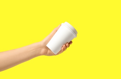 Woman holding takeaway paper coffee cup on yellow background, closeup