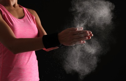 Photo of Young woman applying chalk powder on hands against dark background