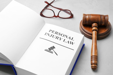 Photo of Book with words PERSONAL INJURY LAW, gavel and glasses on grey background