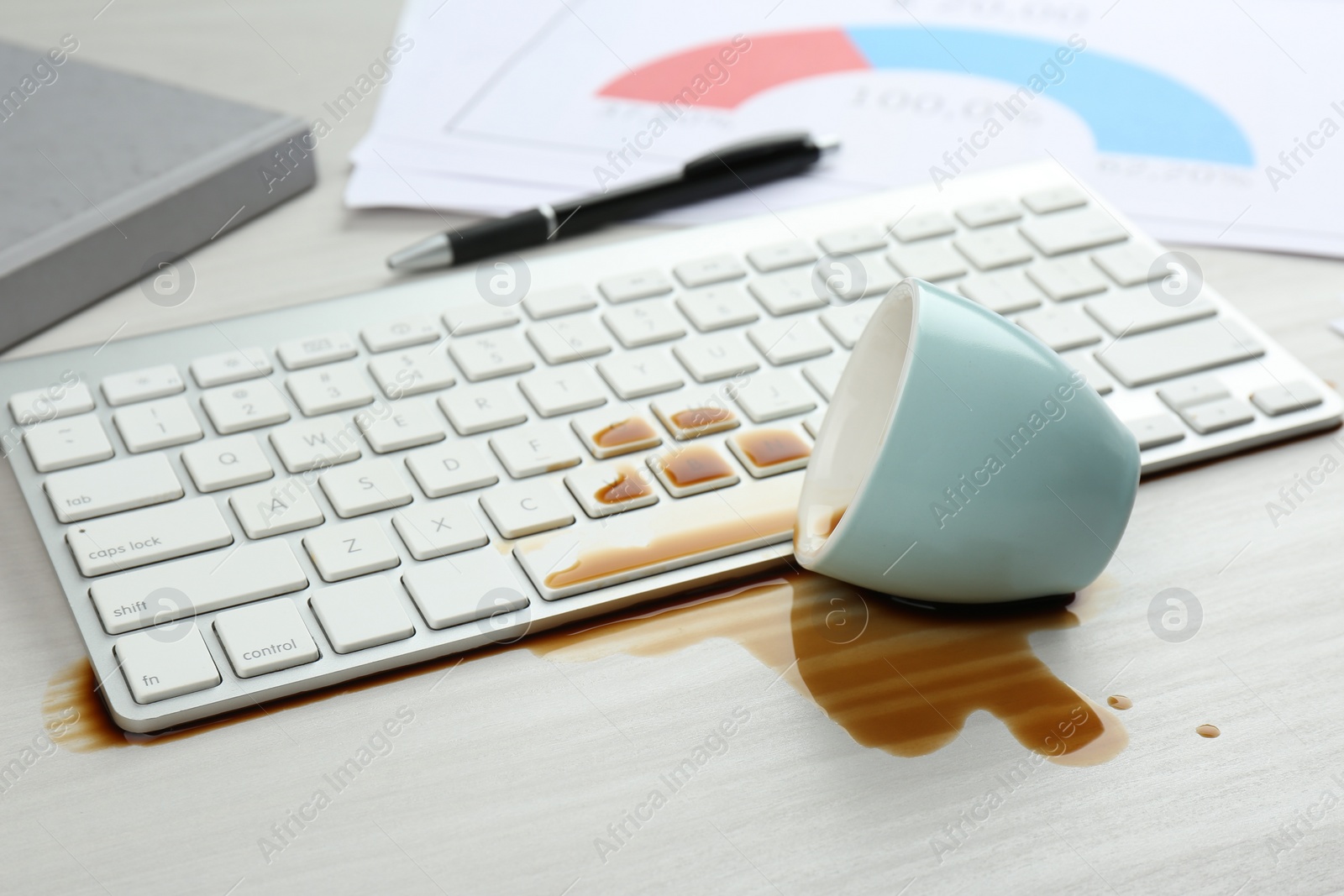 Photo of Cup of coffee spilled over computer keyboard on white wooden table