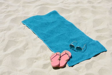 Photo of Soft blue beach towel, pink flip flops and sunglasses on sand. Space for text