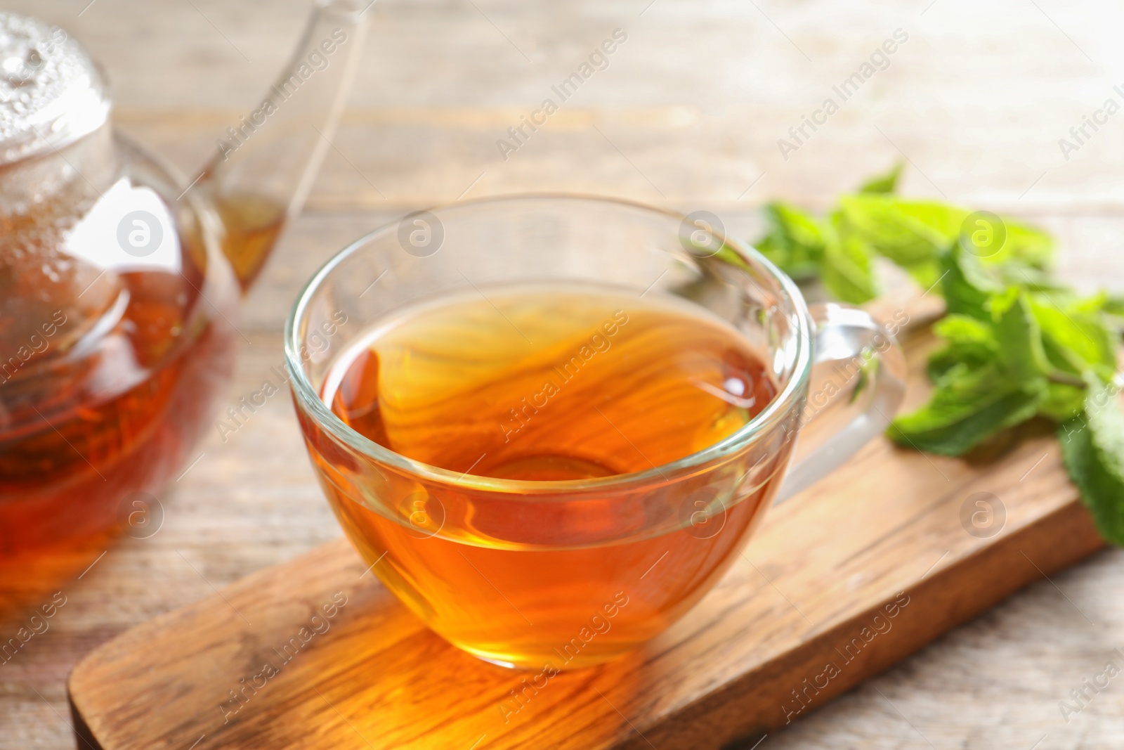 Photo of Cup with hot aromatic mint tea on wooden board