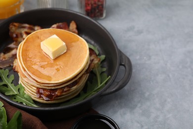Photo of Tasty pancakes with butter, fried bacon and fresh arugula on grey table. Space for text