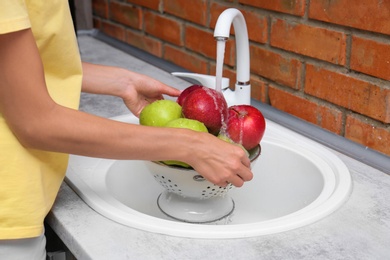 Photo of Woman washing fresh apples in kitchen sink, closeup