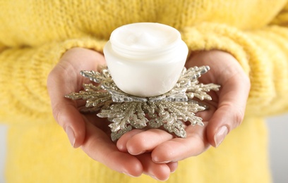 Photo of Woman holding jar with cream and decorative snowflake, closeup. Cosmetic product for winter