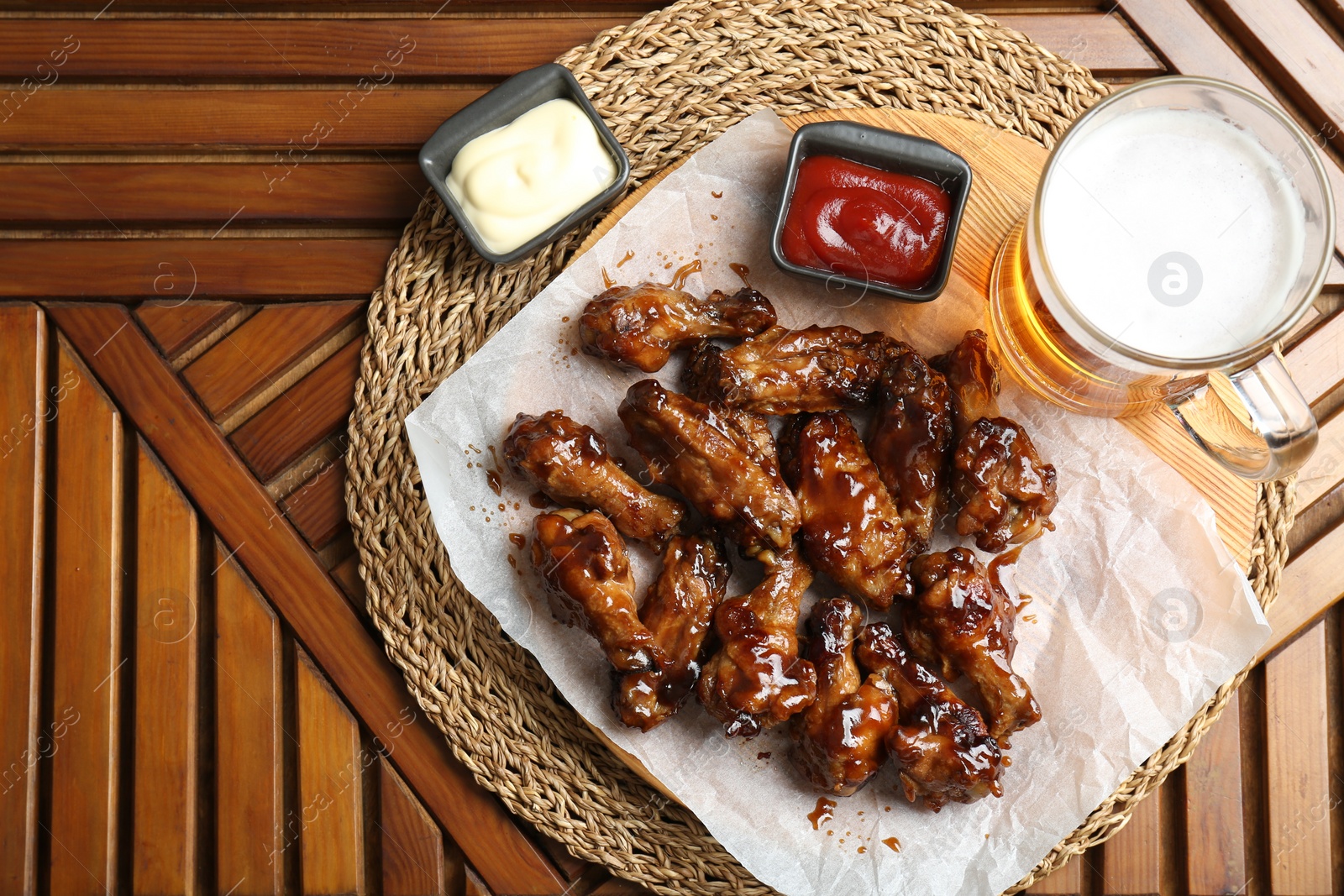 Photo of Tasty chicken wings, mug of beer and sauces on wooden table, flat lay with space for text. Delicious snack