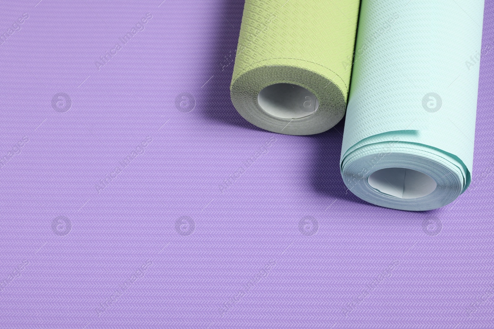 Photo of Two colorful wallpaper rolls on violet sample, above view. Space for text