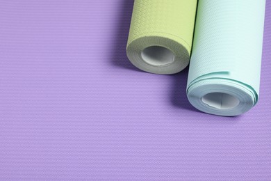 Two colorful wallpaper rolls on violet sample, above view. Space for text