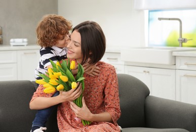 Little son congratulating his mom with Mother`s day at home, space for text. Woman holding bouquet of yellow tulips