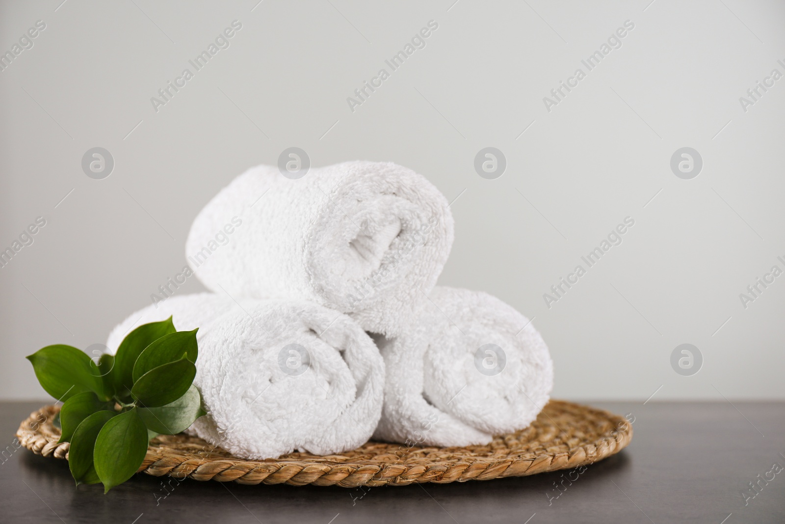 Photo of Clean rolled bath towels, green branch and wicker mat on dark grey table