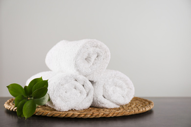 Photo of Clean rolled bath towels, green branch and wicker mat on dark grey table