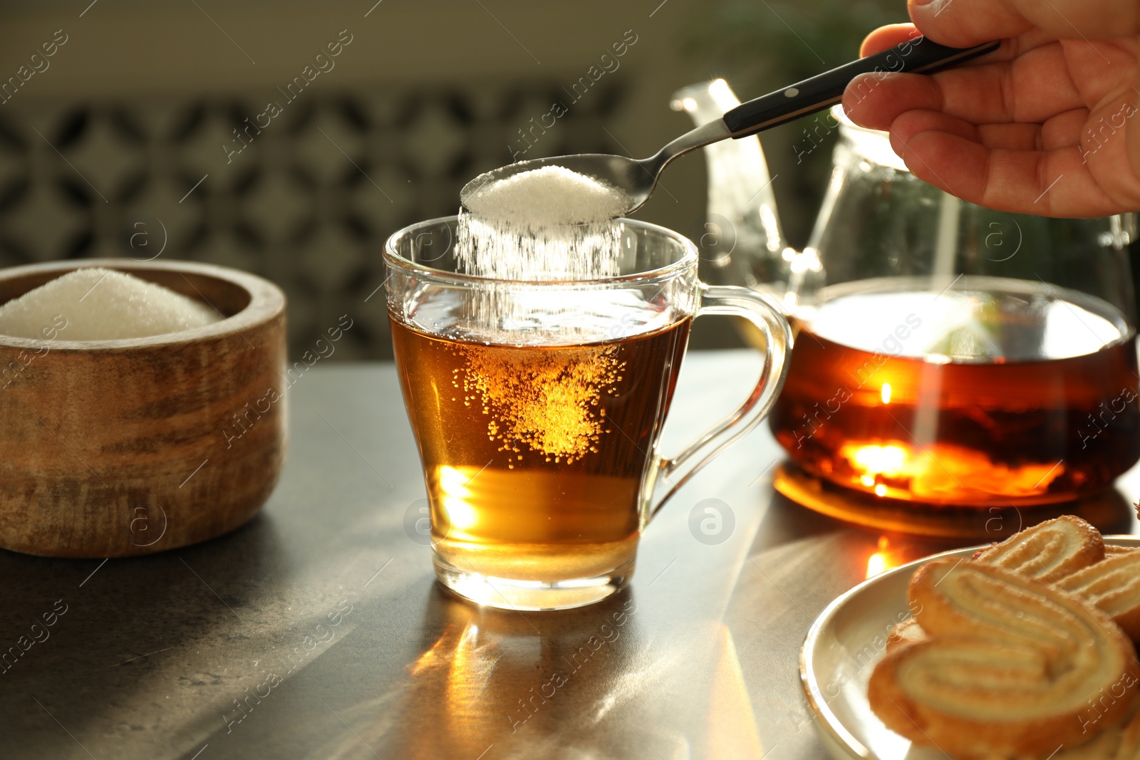 Photo of Woman adding sugar into cup of tea at dark table, closeup