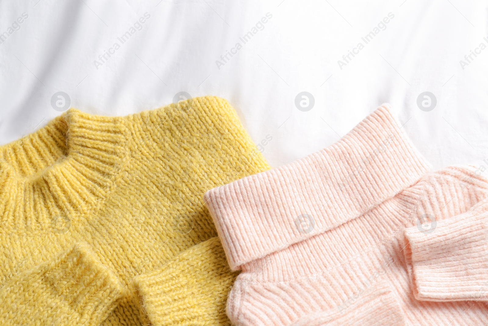 Photo of Stylish knitted sweaters on white fabric, flat lay