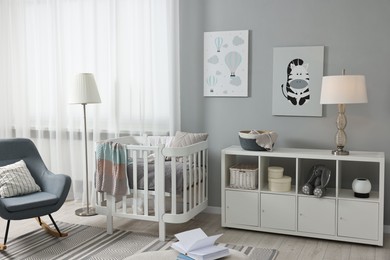 Newborn baby room interior with stylish furniture, comfortable crib and pictures of on wall