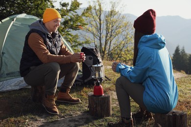 Photo of Young couple drinking coffee near camping tents in mountains