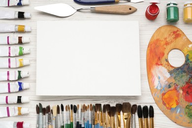 Photo of Blank canvas, brushes, palette and paints on white wooden table, flat lay. Space for text