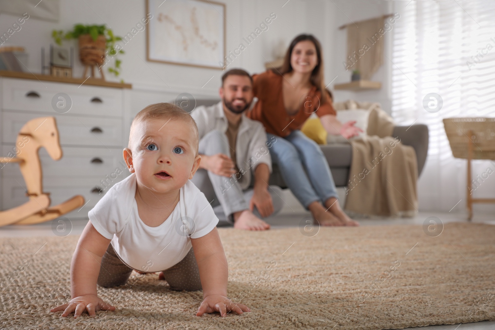 Photo of Happy parents watching their baby crawl on floor at home