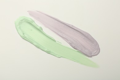 Photo of Strokes of green and purple color correcting concealers on white background, top view