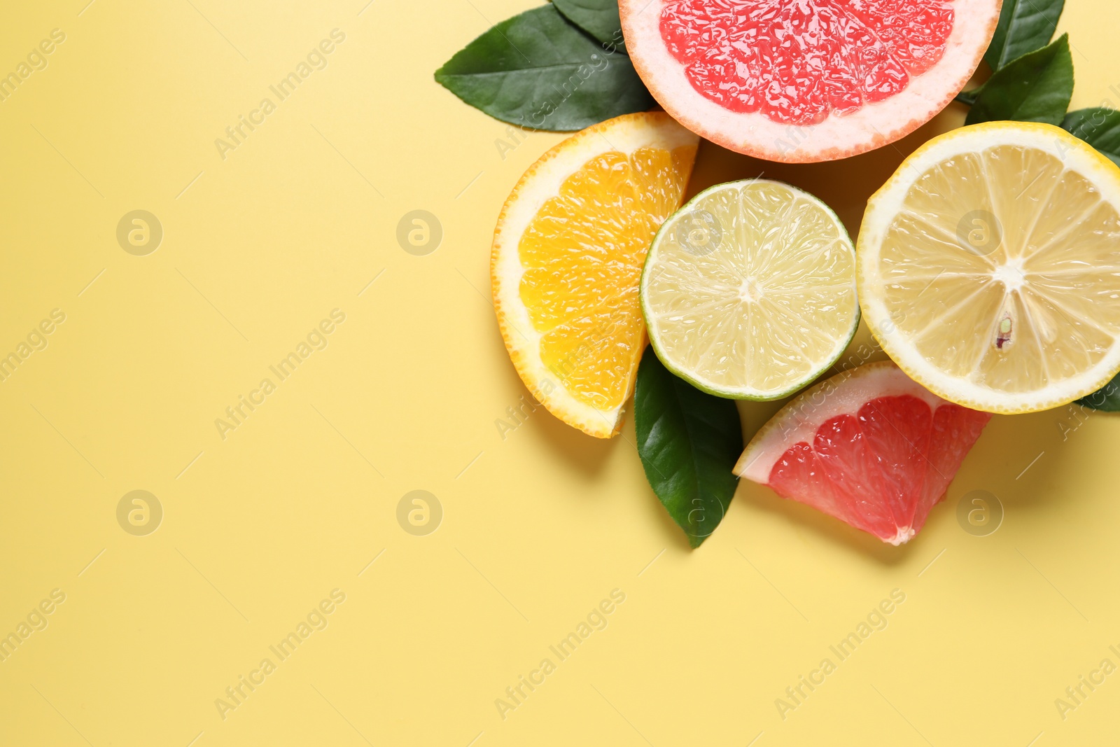 Photo of Different cut citrus fruits and leaves on yellow table, flat lay. Space for text