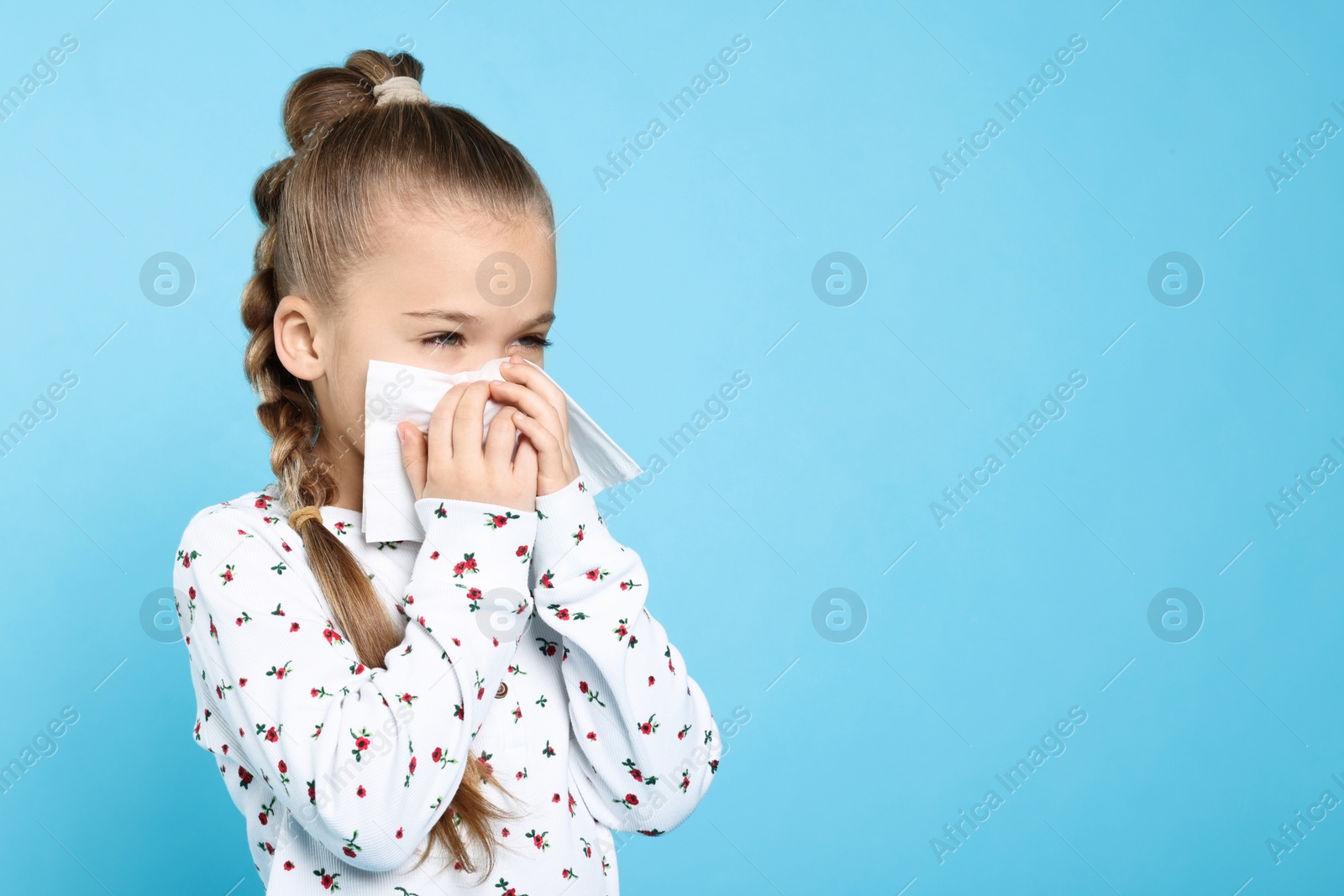 Photo of Sick girl blowing nose in tissue on turquoise background, space for text. Cold symptoms