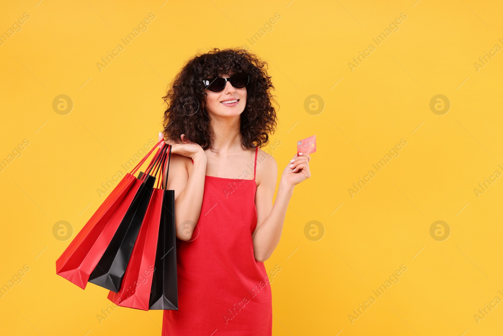 Photo of Happy young woman with shopping bags and credit card on yellow background