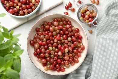 Bowls full of ripe gooseberries on light grey marble table, flat lay