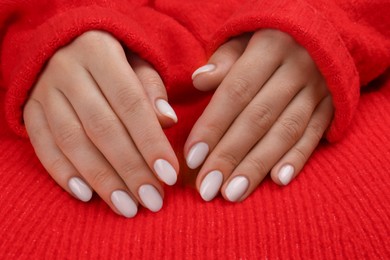 Photo of Woman with white polish on nails on red knitted background, closeup