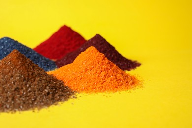 Photo of Heaps of different bright food coloring on yellow background, closeup