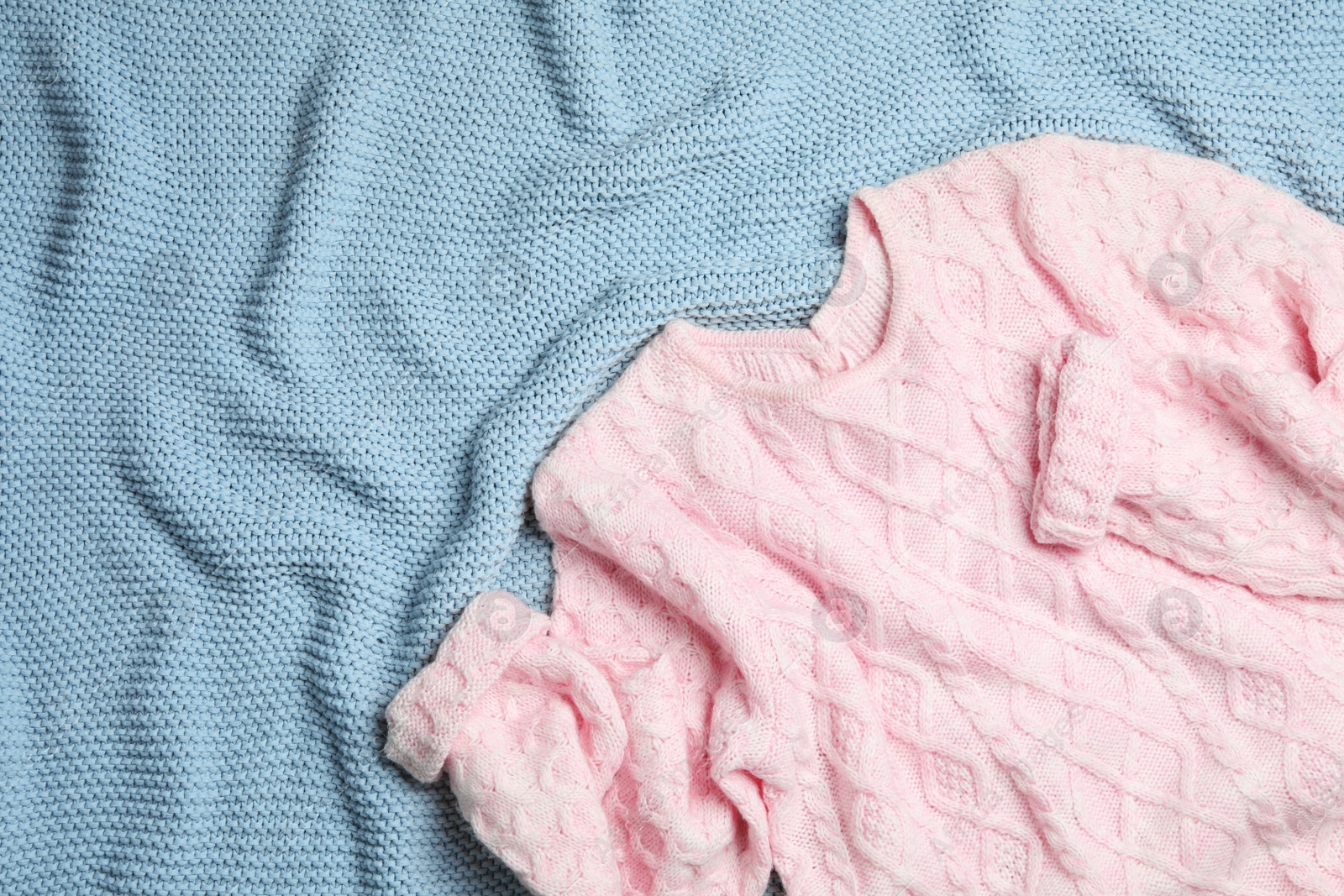 Photo of Warm pink knitted sweater on light blue blanket, flat lay