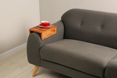 Photo of Cup of tea on sofa with wooden armrest table in room. Interior element