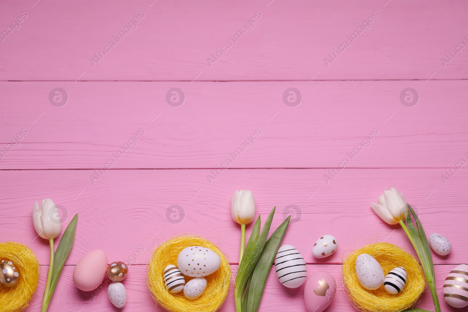 Photo of Flat lay composition of painted Easter eggs and tulip flowers on pink wooden table. Space for text