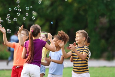 Photo of Cute little children playing with soap bubbles in park