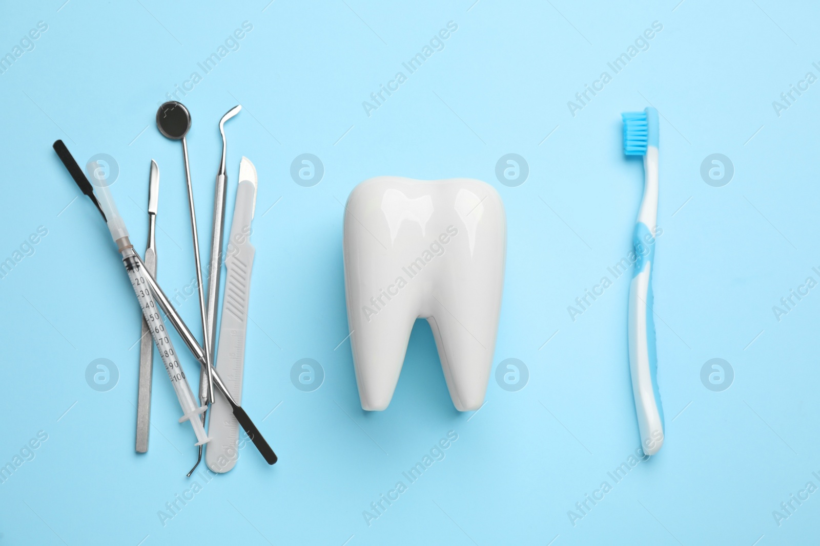 Photo of Tooth shaped holder, brush and dentist's tools on light blue background, flat lay