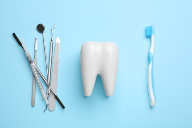 Photo of Tooth shaped holder, brush and dentist's tools on light blue background, flat lay