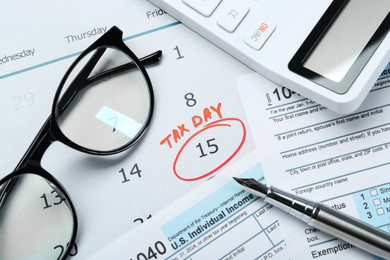 Tax day. Calendar with date reminder, documents, glasses, pen and calculator on table, flat lay