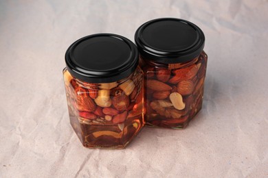 Photo of Jars with different nuts and honey on beige background