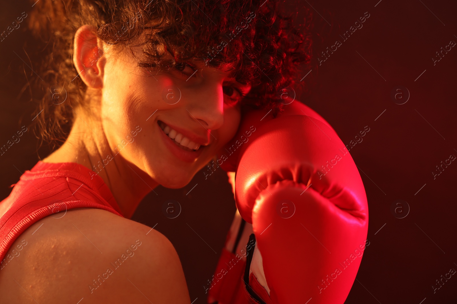 Photo of Beautiful young woman with boxing gloves on color background in neon lights, closeup