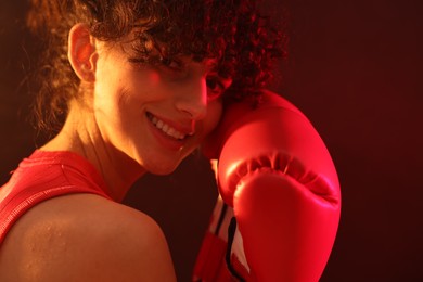 Photo of Beautiful young woman with boxing gloves on color background in neon lights, closeup