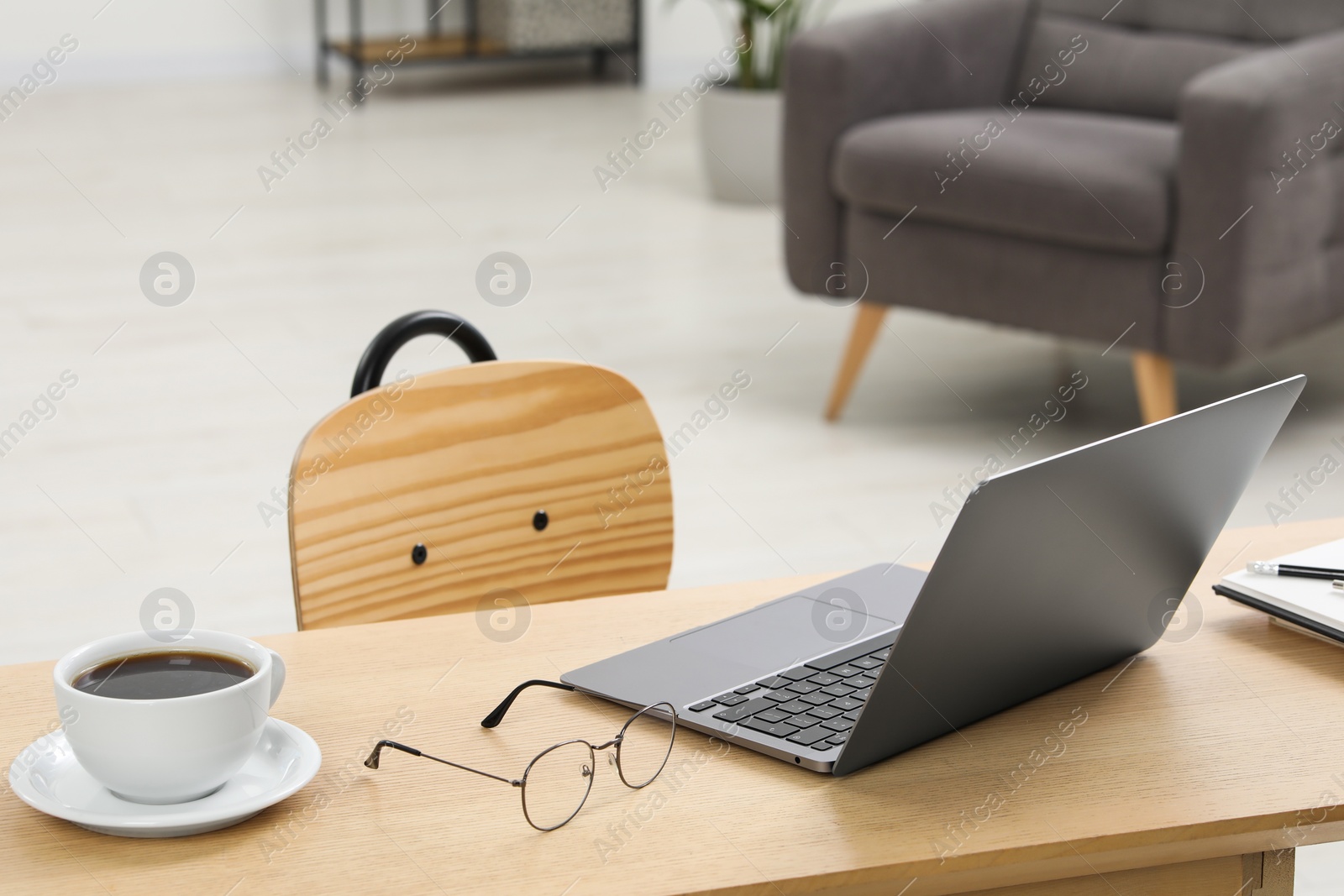 Photo of Home workspace. Laptop, glasses, cup of coffee and stationery on wooden desk in room. Space for text