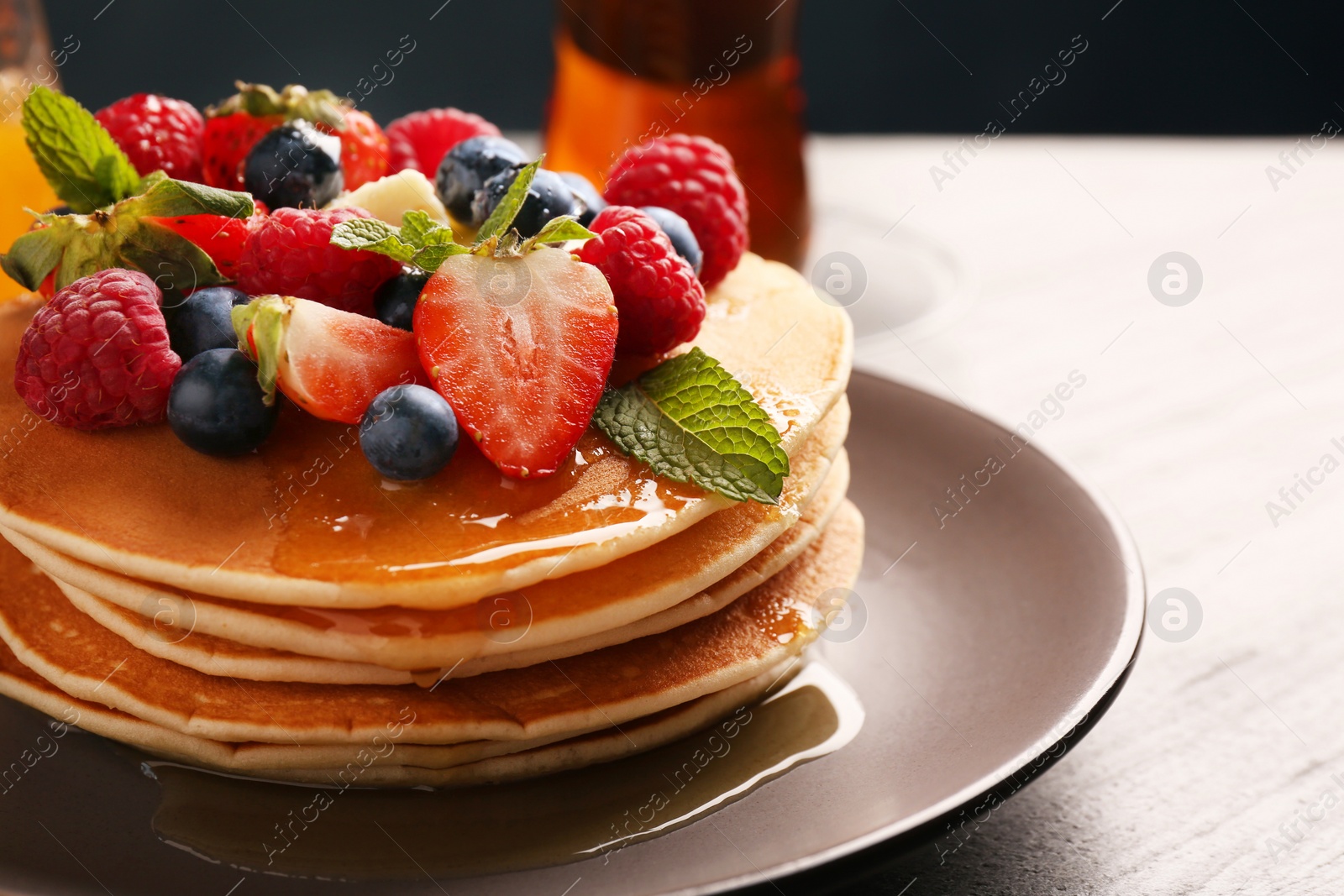 Photo of Delicious pancakes with fresh berries, honey and butter on grey table, closeup