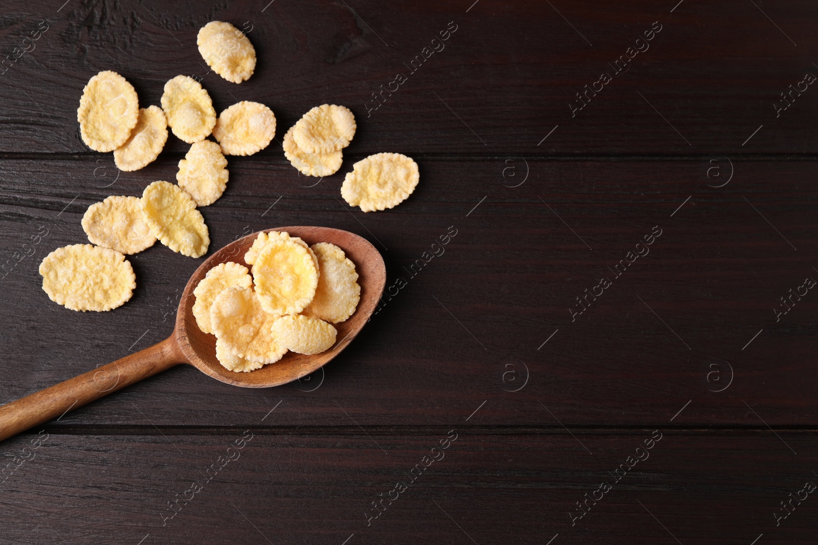 Photo of Spoon and tasty crispy corn flakes on wooden table, flat lay. Space for text