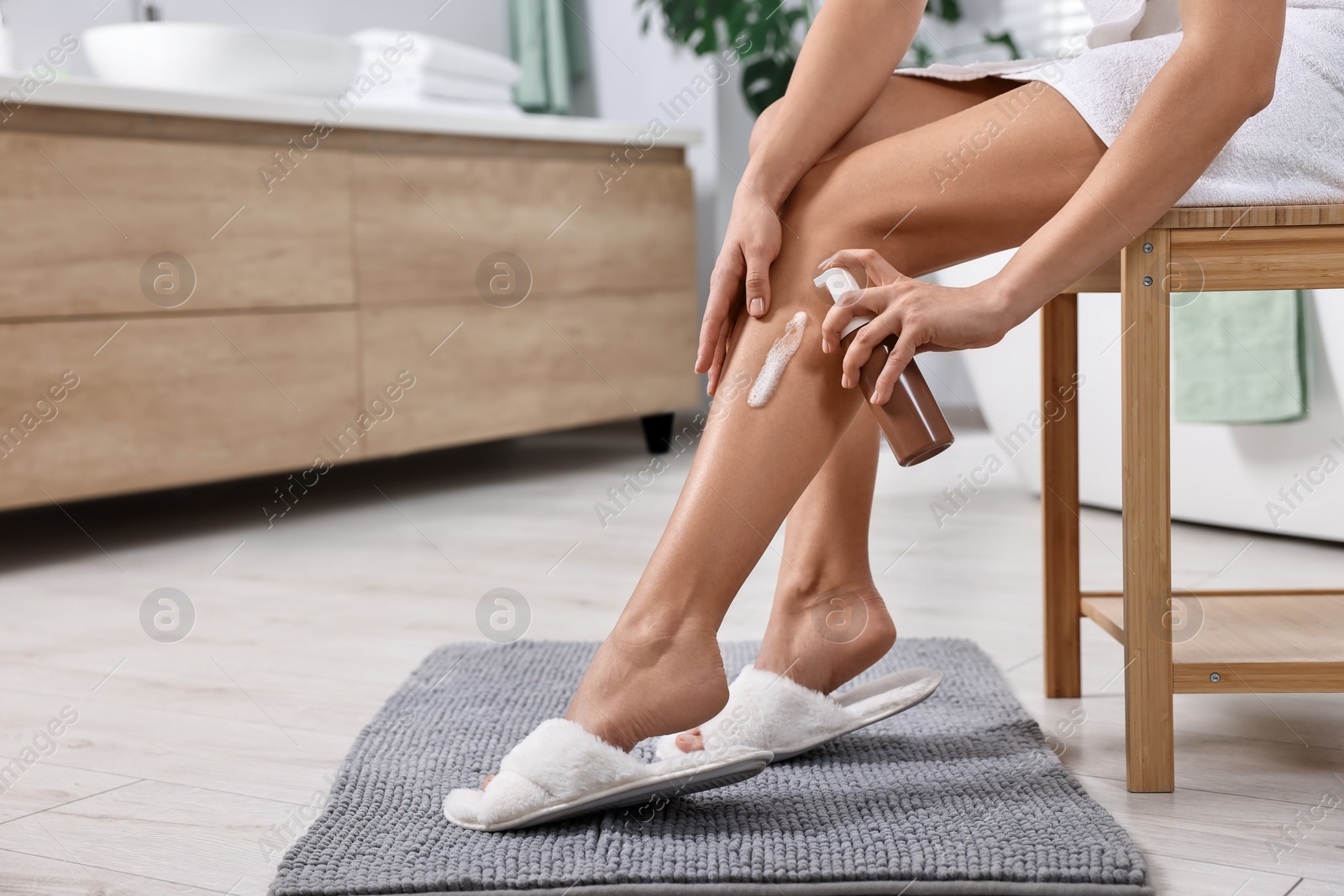 Photo of Woman applying self-tanning product onto leg on wooden chair in bathroom, closeup. Space for text