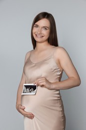 Pregnant woman with ultrasound picture of baby on light grey background