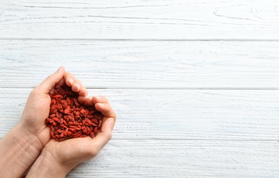 Photo of Woman holding goji berries on white wooden background, top view with space for text. Heart health