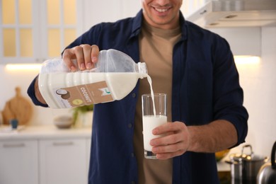 Image of Man pouring coconut milk from gallon bottle into glass in kitchen, closeup. Vegan product