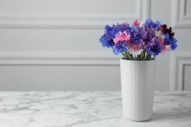 Photo of Bouquet of beautiful cornflowers in vase on white marble table. Space for text